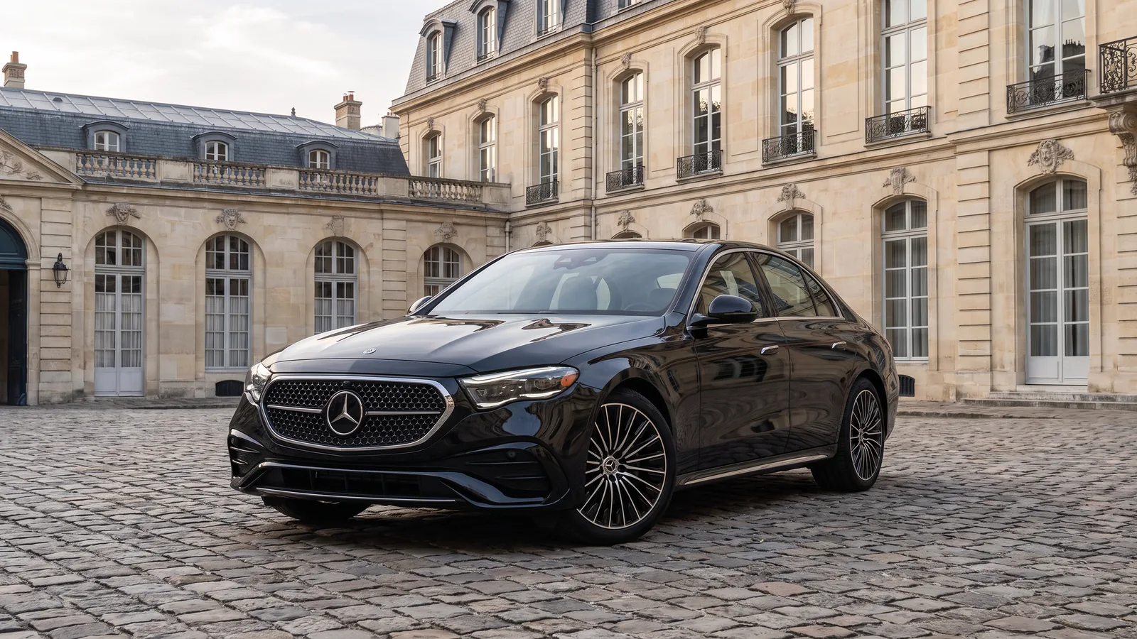 Mercedes-Benz Classe E noire, trois quarts avant, dans la cour pavée d'un hôtel particulier parisien